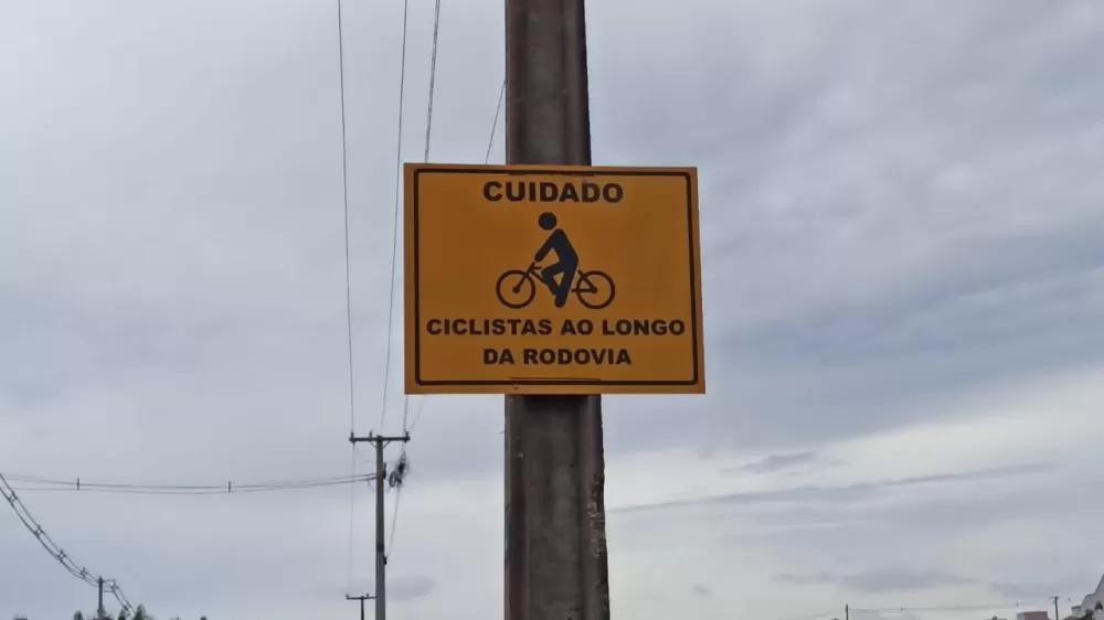 Estrada rural sinalizada com placa “Cuidado, ciclista”, alertando motoristas sobre a presença de bicicletas. (Foto: Assessoria)