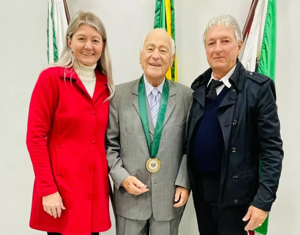 Os vereadores Marciane Specht, autora da proposição, e Valdir Sachser, presidente da Casa, ladeiam o homenageado, professor Tarsizo de Oliveira. (Foto: Cristiano Viteck)